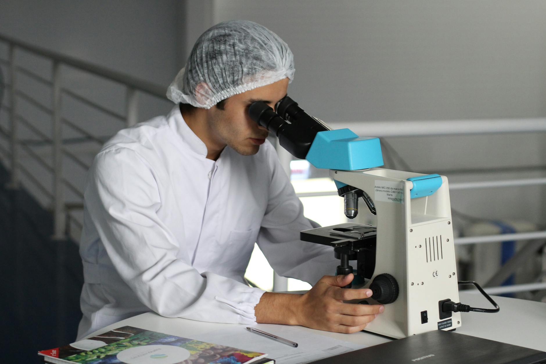A man in a white lab coat examines a sample through a microscope in a laboratory setting.